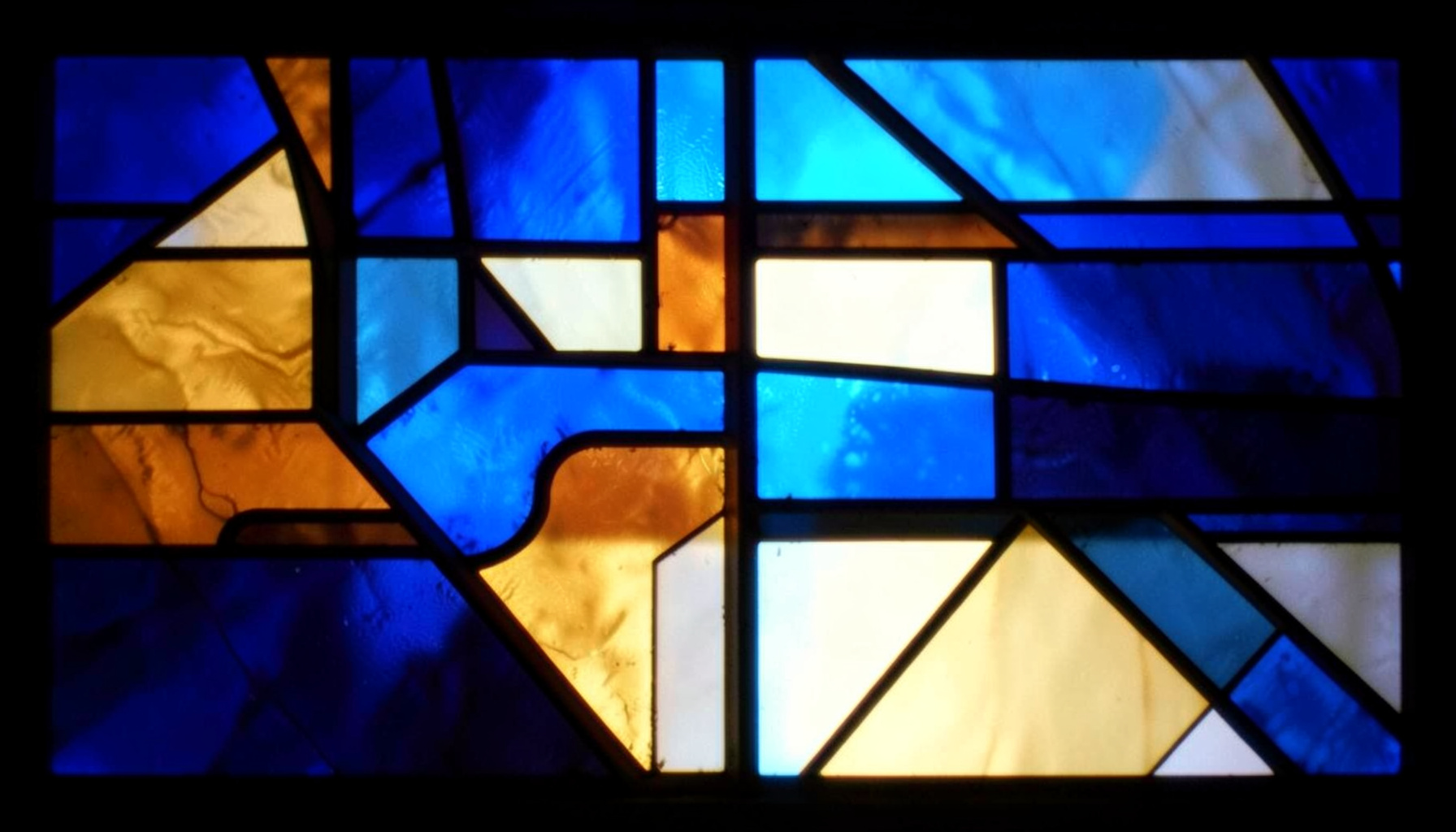 A stained-glass composition with bold leaded segments in deep blues, warm amber, and soft ivory, forming abstract geometric shapes that evoke structured logic and functional precision.